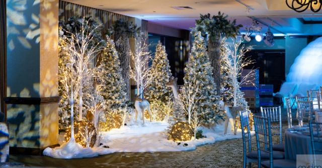 A winter wonderland decor at a Christmas party featuring snow-covered trees, illuminated deer, and glowing orbs