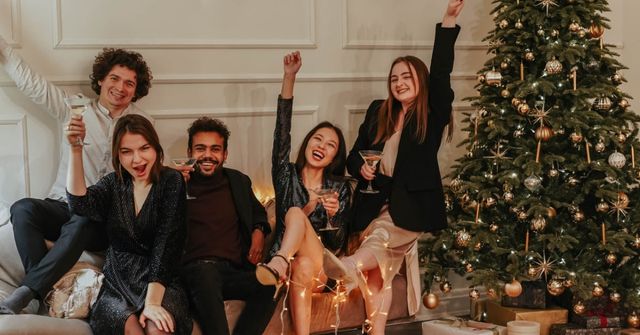 Group of coworkers wearing proper work Christmas party outfits socialize in a corner of the venue