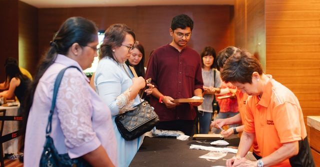 A group of event attendees stand at packaging counter where workshop facilitators help them pack their herbal sachets