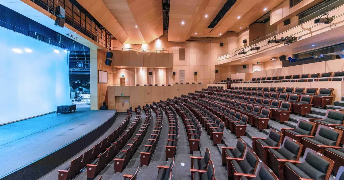 A spacious, empty theater with rows of cushioned seats and a large stage, suitable for confernec planning