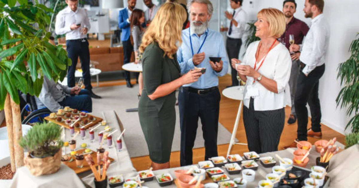 A group of conference attendees mingle and engage in conversations near buffet tables 