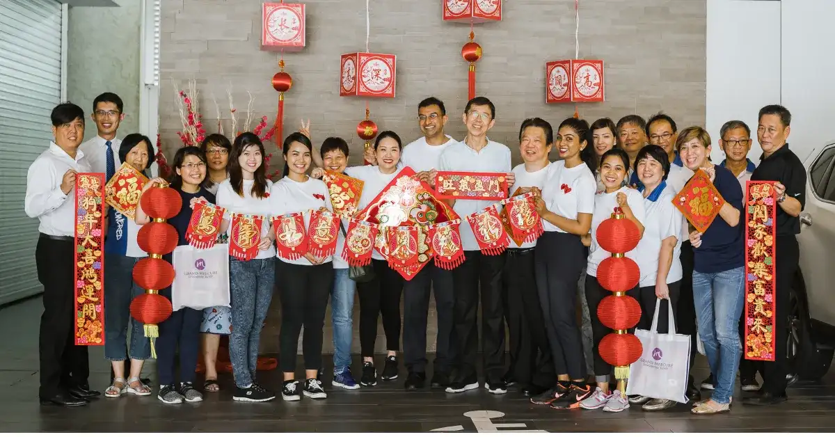 A group of coworkers stand smiling, holding red Chinese New Year decorations and lanterns