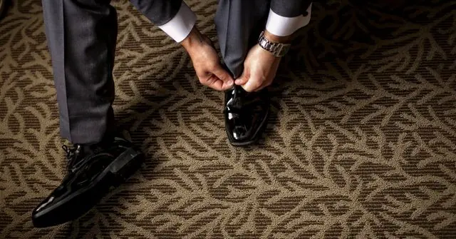 A man is putting on his leather shoes, completing company Christmas party outfit 