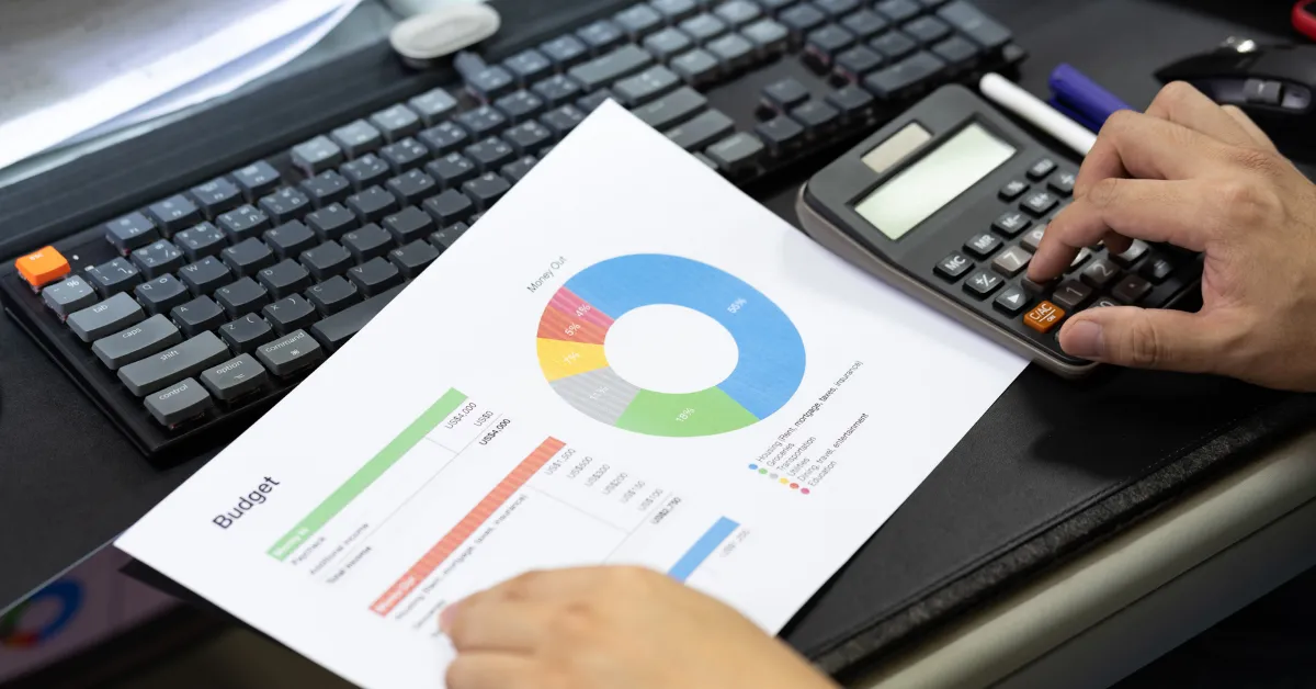 A person uses a calculator and a corporate event budget sheet with a colorful pie chart