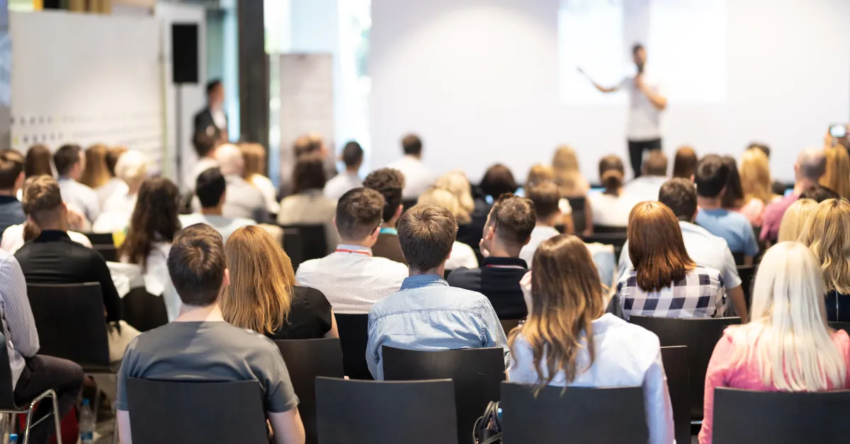 A diverse audience attentively watches a speaker at an internal corporate event