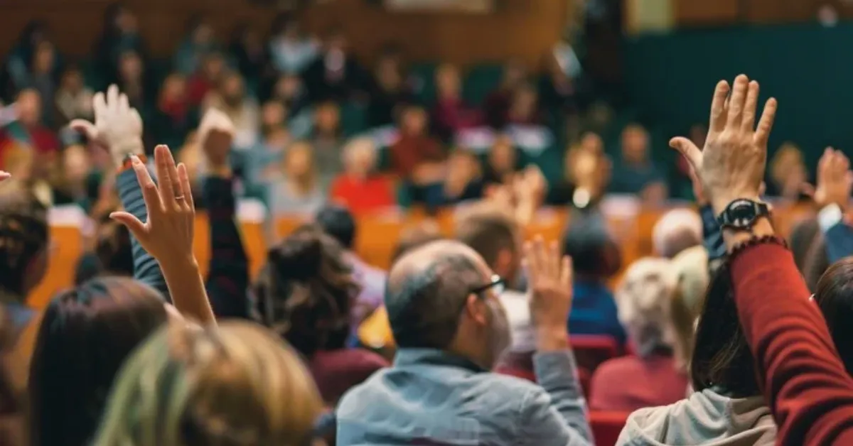 Audience at a seminar raise their hands, suggesting active participation
