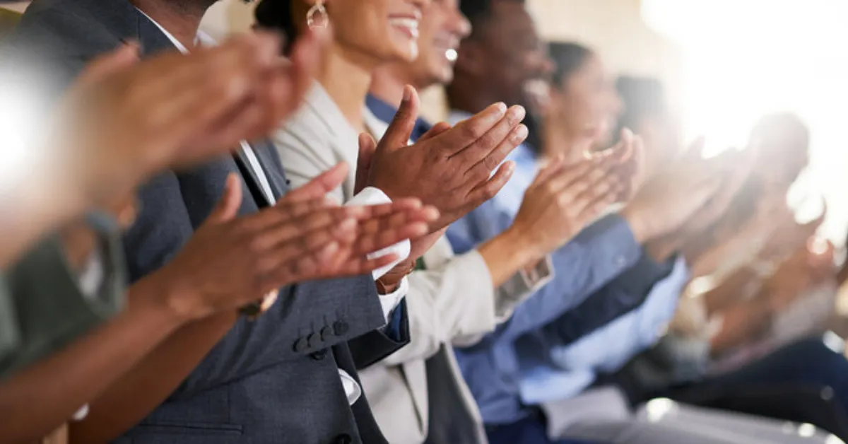A diverse group of people sits in a row, actively clapping during “cluster clap" icebreaker activity