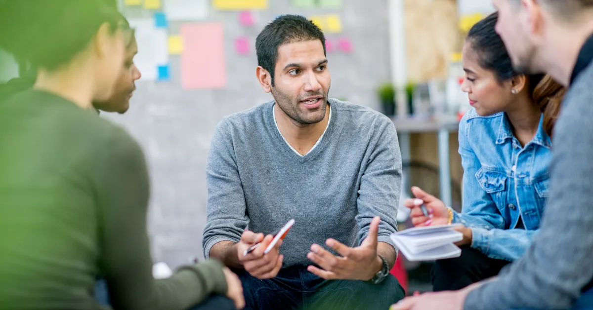 A group of five colleagues sit in a circle, discussing their upcoming seminar objectives