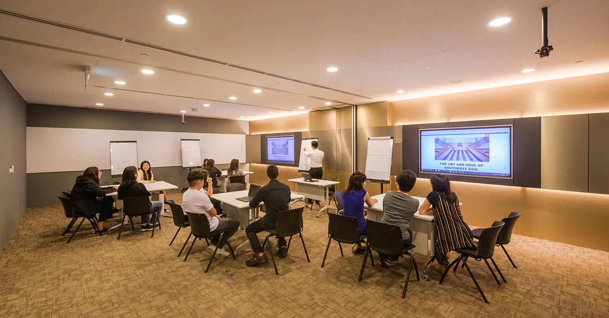 A modern seminar room with people seated at tables, watching a presentation