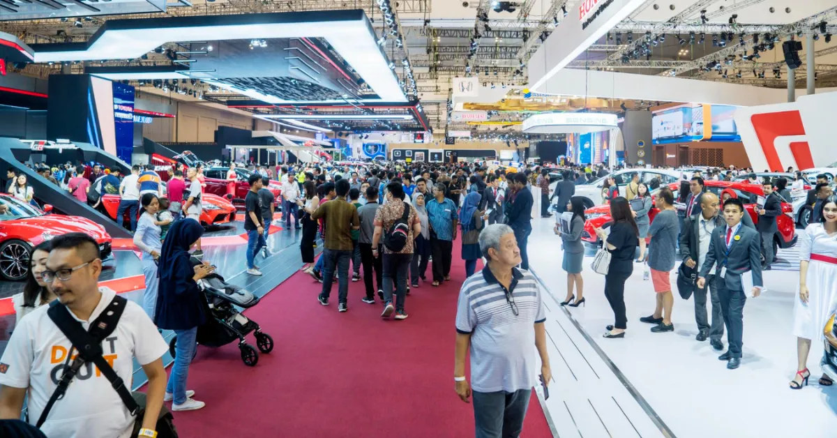 A bustling auto show with a large crowd, casually engaging with exhibits